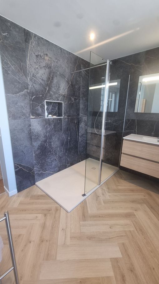 Salle de bains moderne avec murs en marbre noir, cabine de douche en verre et sol en parquet à chevrons
