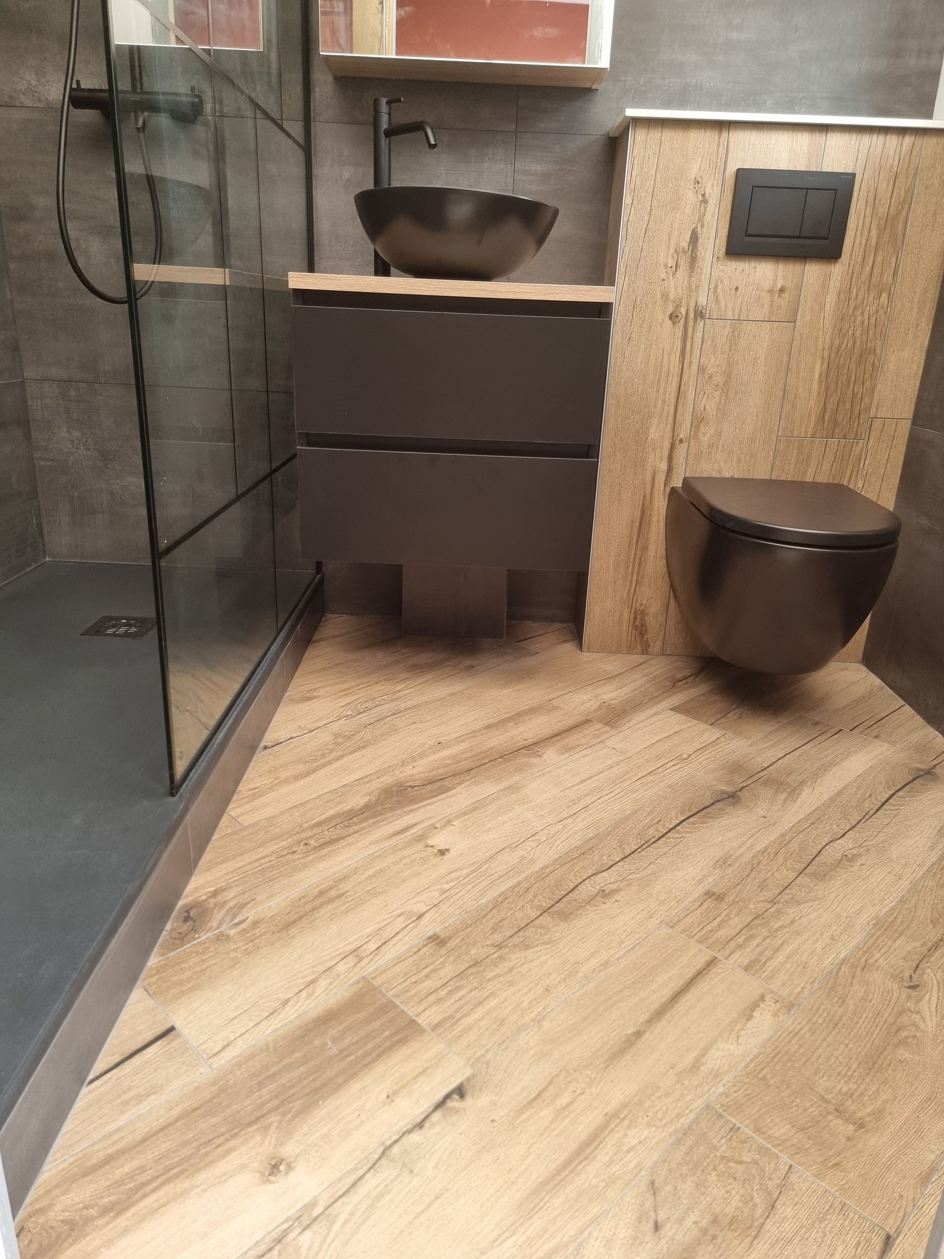 Coin salle de bains moderne avec lavabo, WC suspendu, douche en verre et carrelage imitation bois au sol.