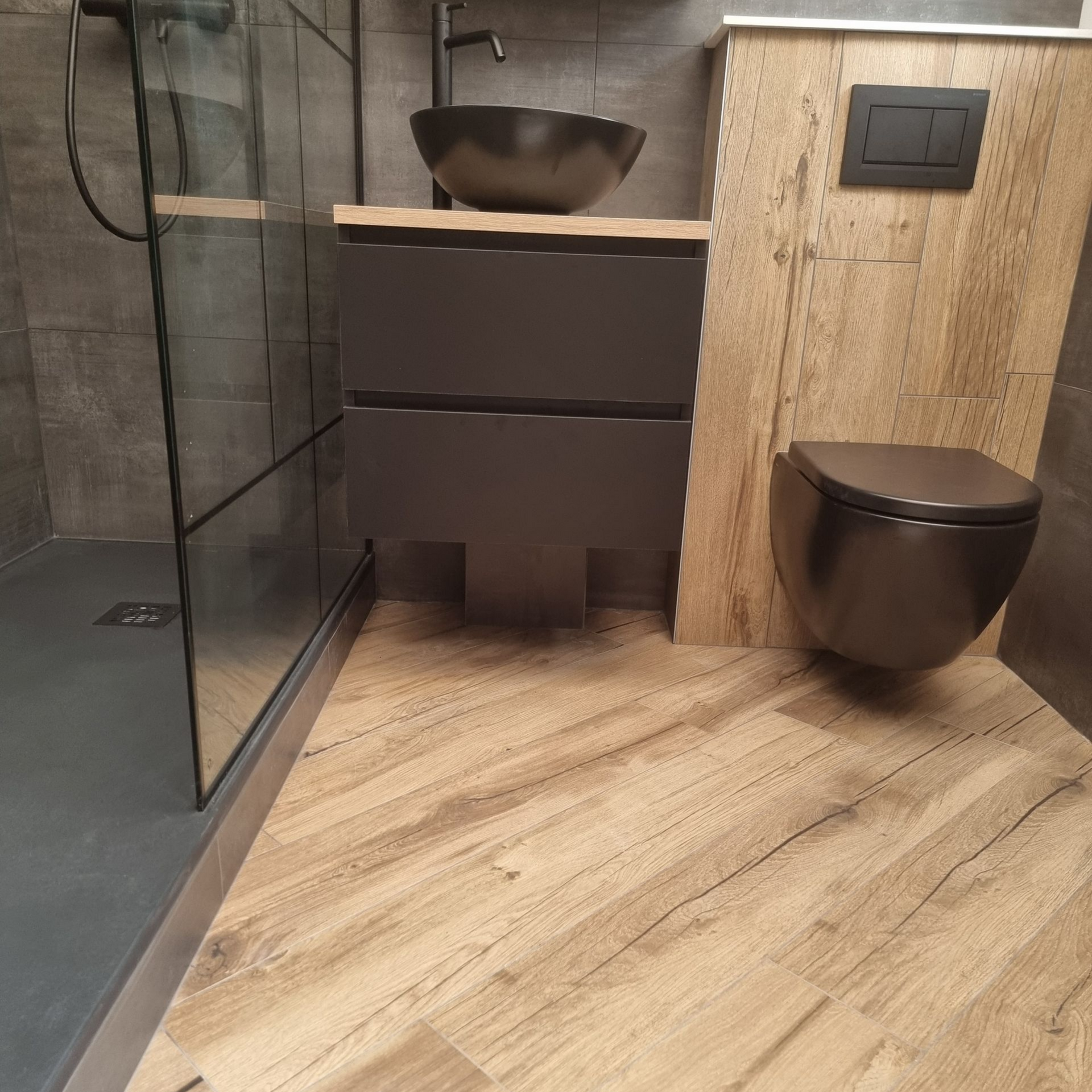Salle de bains moderne avec douche en verre, meuble-lavabo suspendu, vasque et toilettes suspendues sur sol imitation bois
