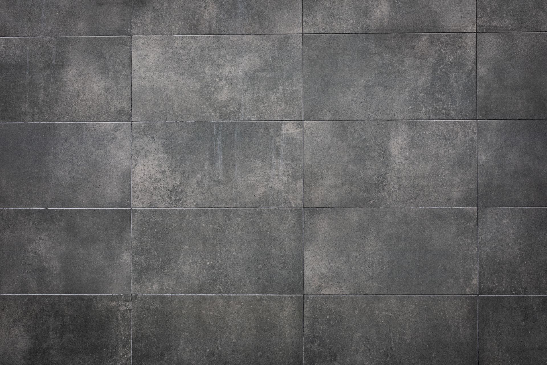 Mur carrelé de carreaux de béton gris à surface rugueuse et texturée, avec des joints horizontaux.