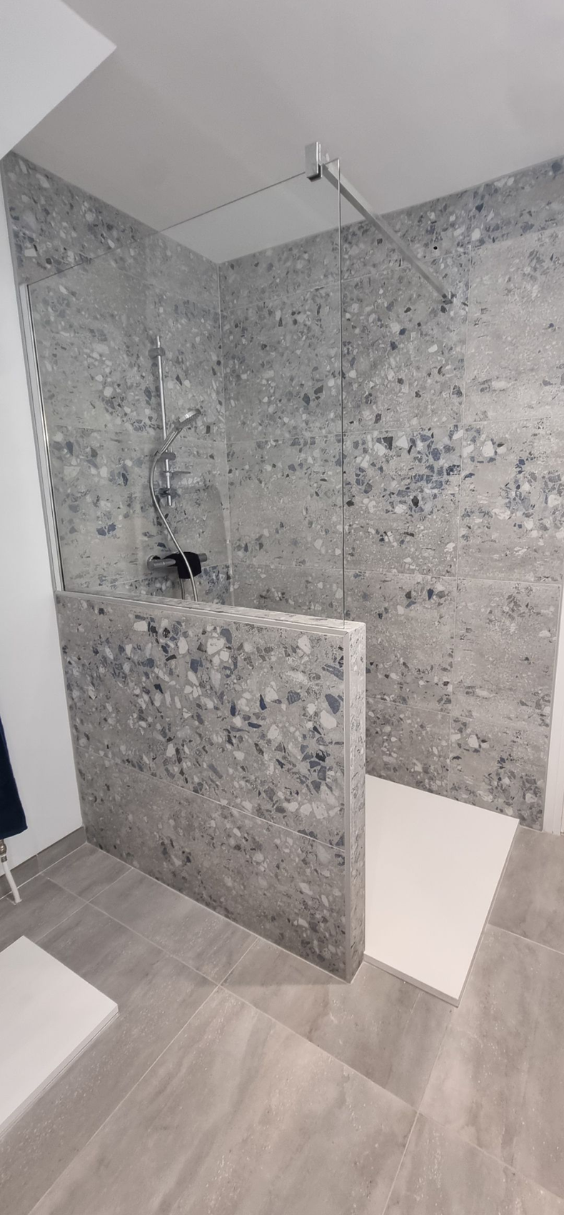 Cabine de douche moderne carrelée de gris avec paroi partiellement vitrée et murs et sol carrelés.