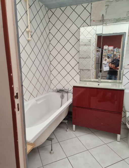Salle de bains avec baignoire blanche, meuble-lavabo et miroir rouges, carrelage mural à motif losanges et sol carrelé