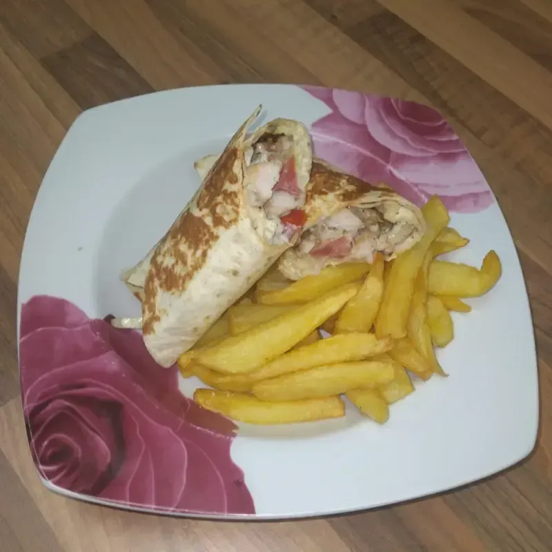 Sándwich envuelto en papel de aluminio y papas fritas en un plato decorado con flores.