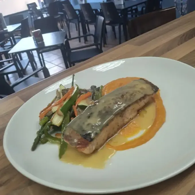 Salmón emplatado con salsa de naranja y verduras sobre una mesa en un restaurante.