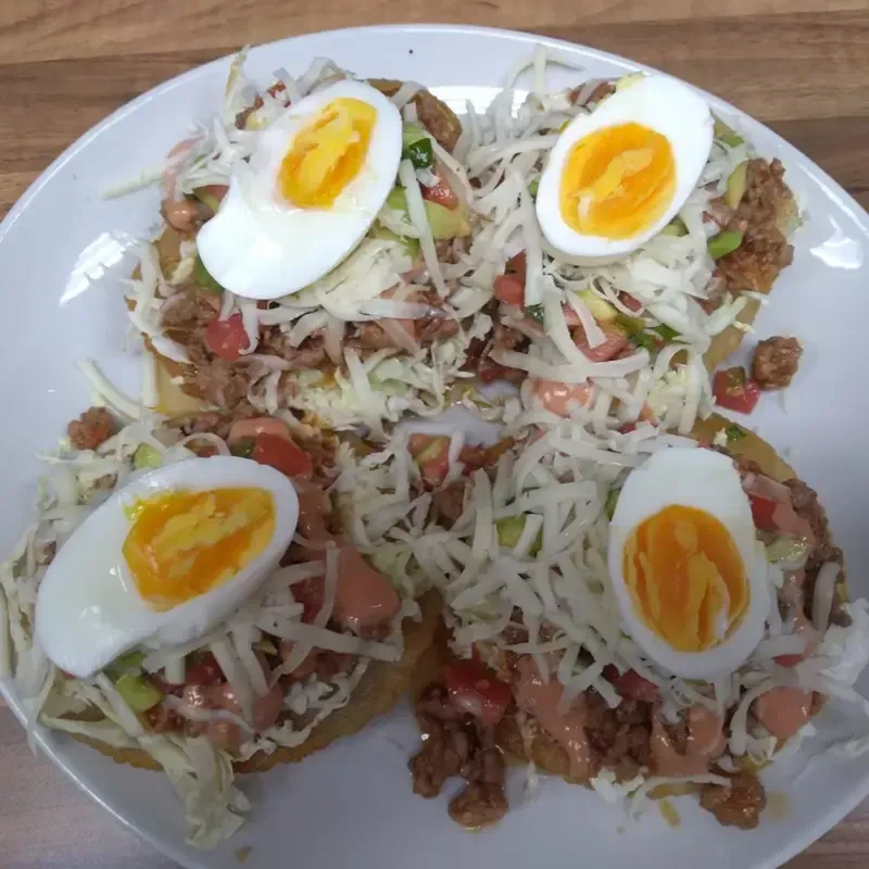 Plato de ensalada desmenuzada cubierta con huevos duros partidos por la mitad y trozos de tomate sobre un plato blanco.