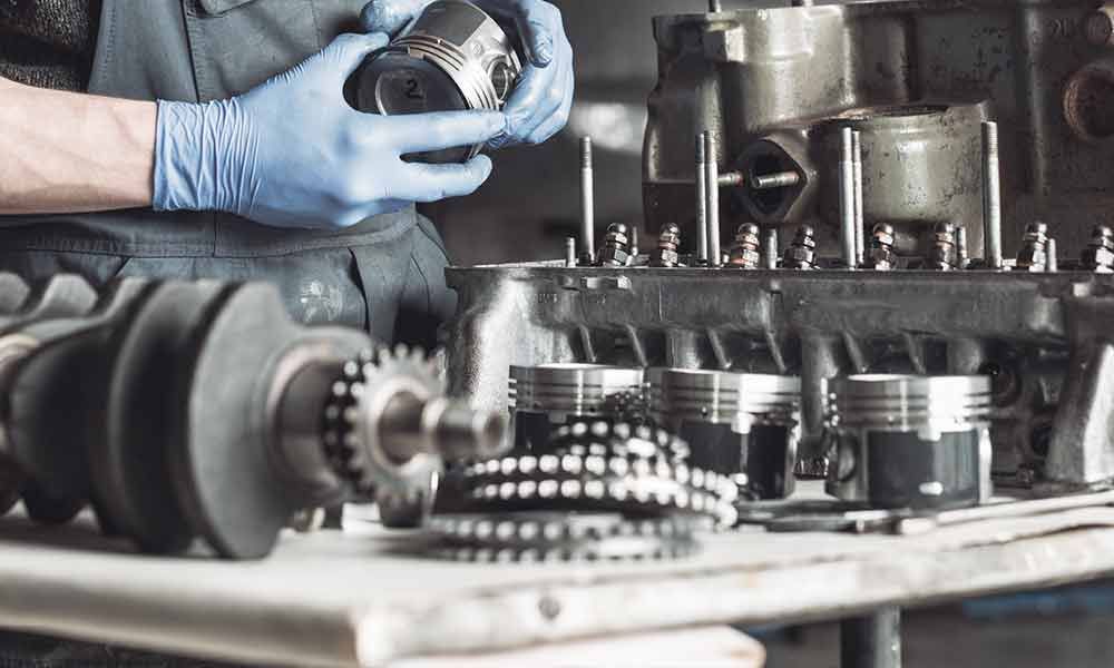 Ein Mechaniker mit blauen Handschuhen arbeitet an einem Motor, umgeben von Teilen auf einem Tisch.