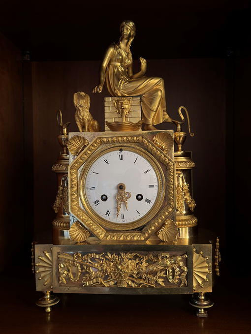 Une horloge de couleur or avec des statuettes dessus.