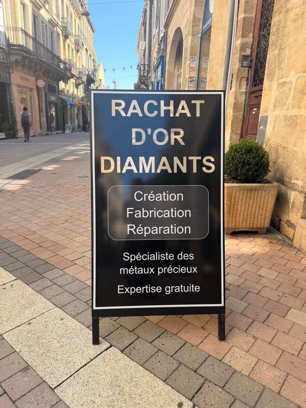 Panneau noir sur le trottoir indiquant Achat d'Or Diamants dans une rue pavée du centre-ville de Bordeaux.