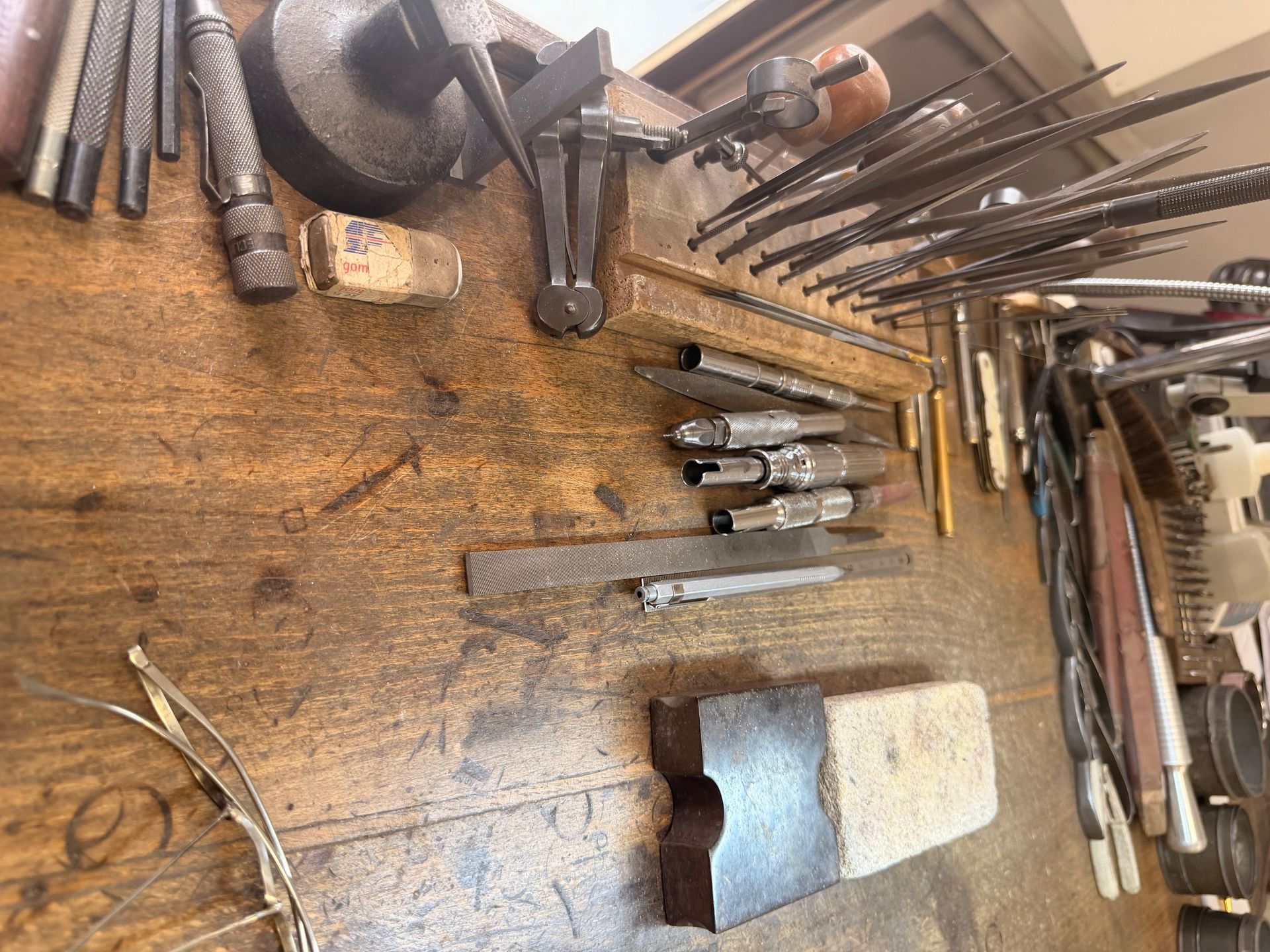 Atelier de joaillerie avec divers forets, poinçons et outils métalliques disposés sur une surface en bois.