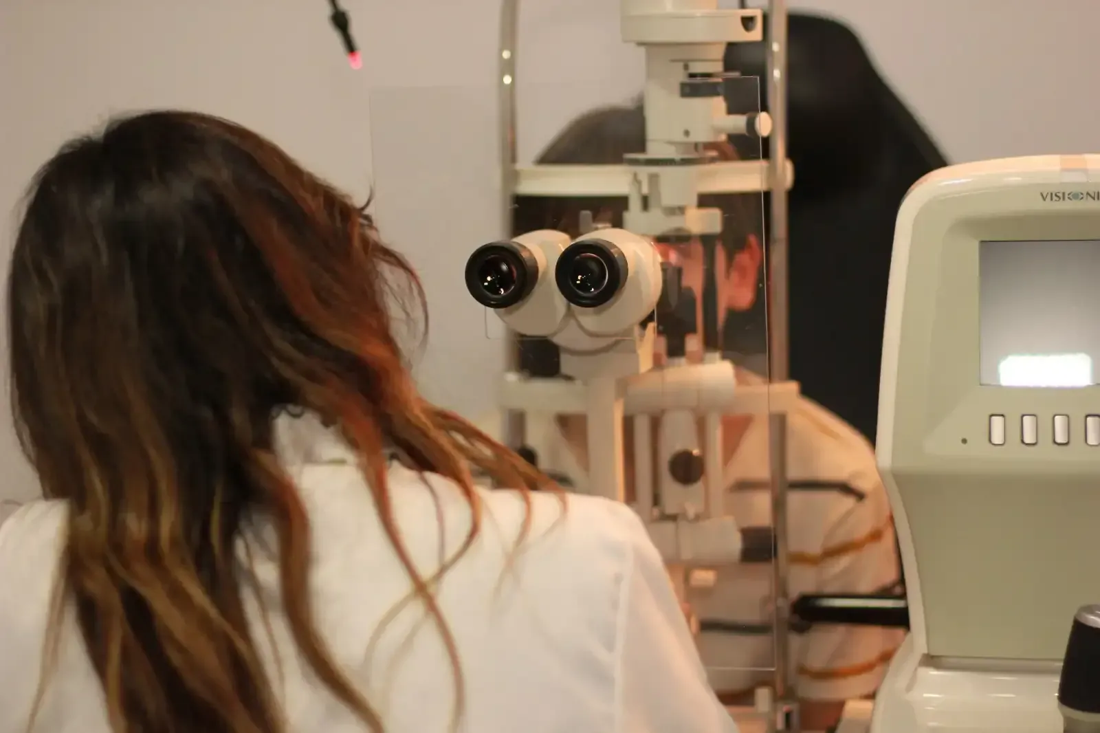 Una mujer con una bata blanca mira a través de un microscopio.
