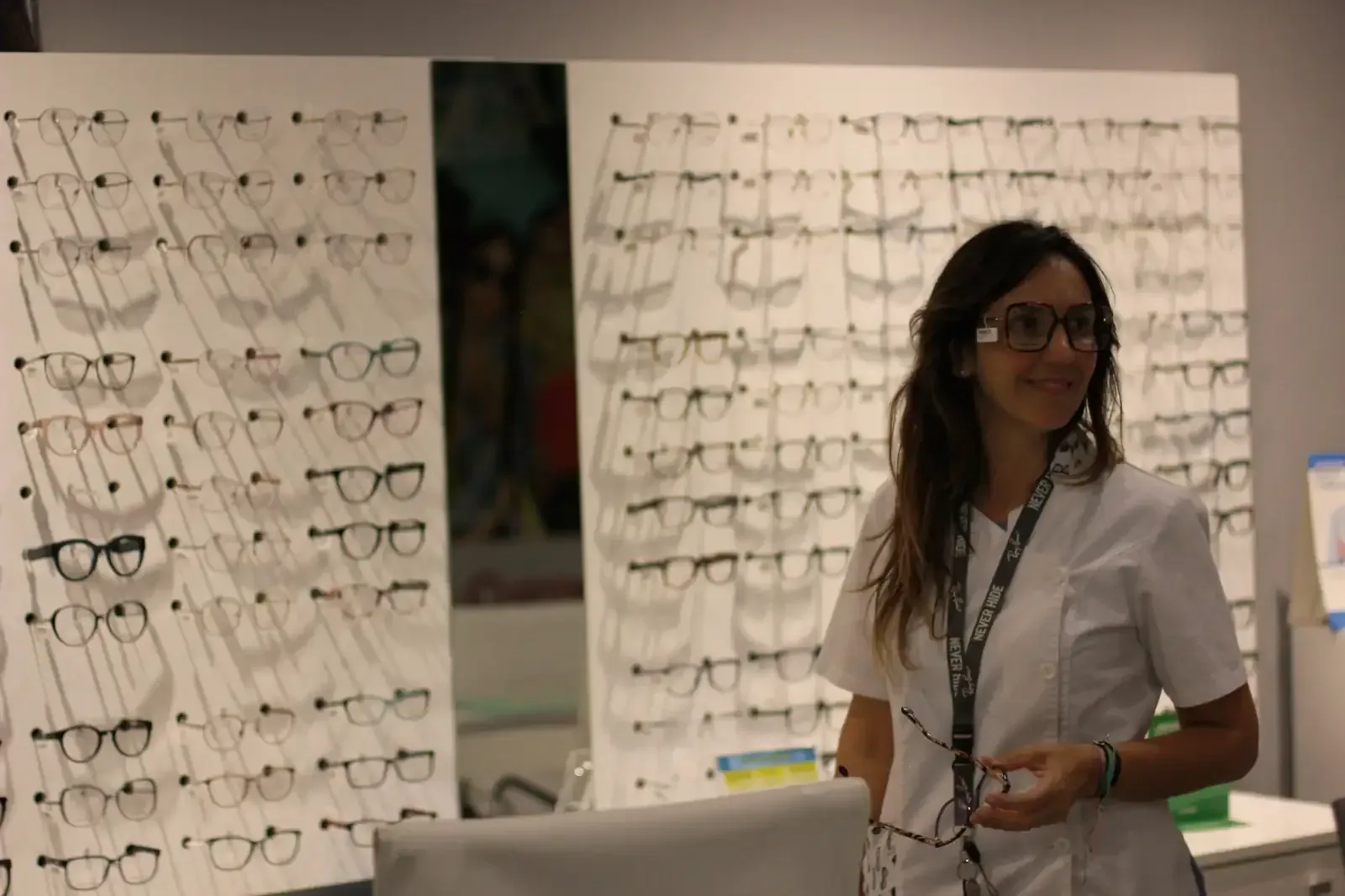 Una mujer que lleva gafas está parada frente a una pared de gafas.