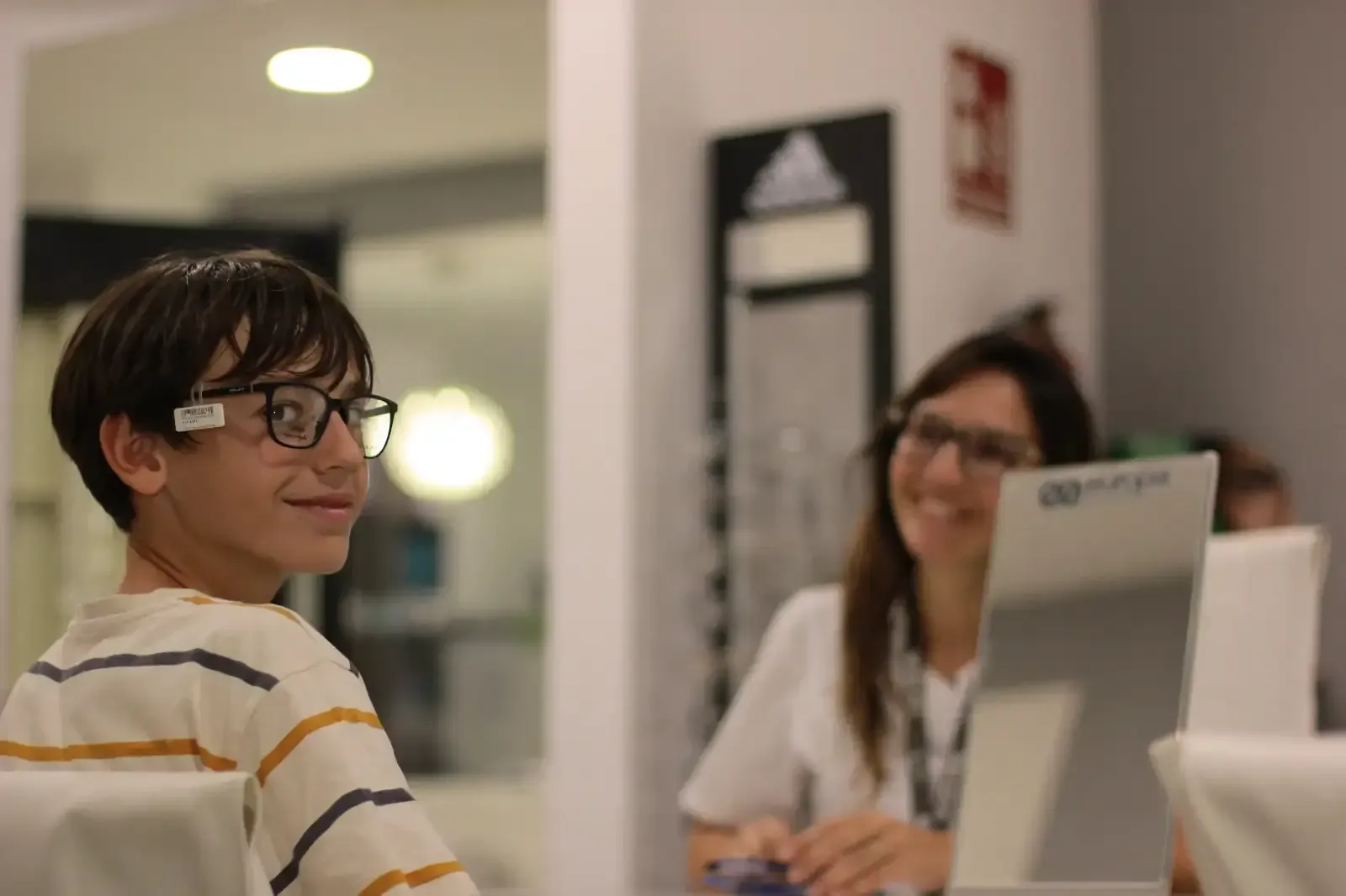 Un niño que lleva gafas está sentado delante de un monitor de computadora.