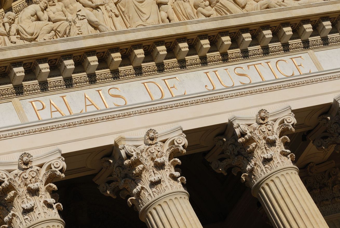 Gros plan sur la façade d'un bâtiment classique avec l'inscription PALAIS DE JUSTICE au-dessus de colonnes en pierre sculptée.