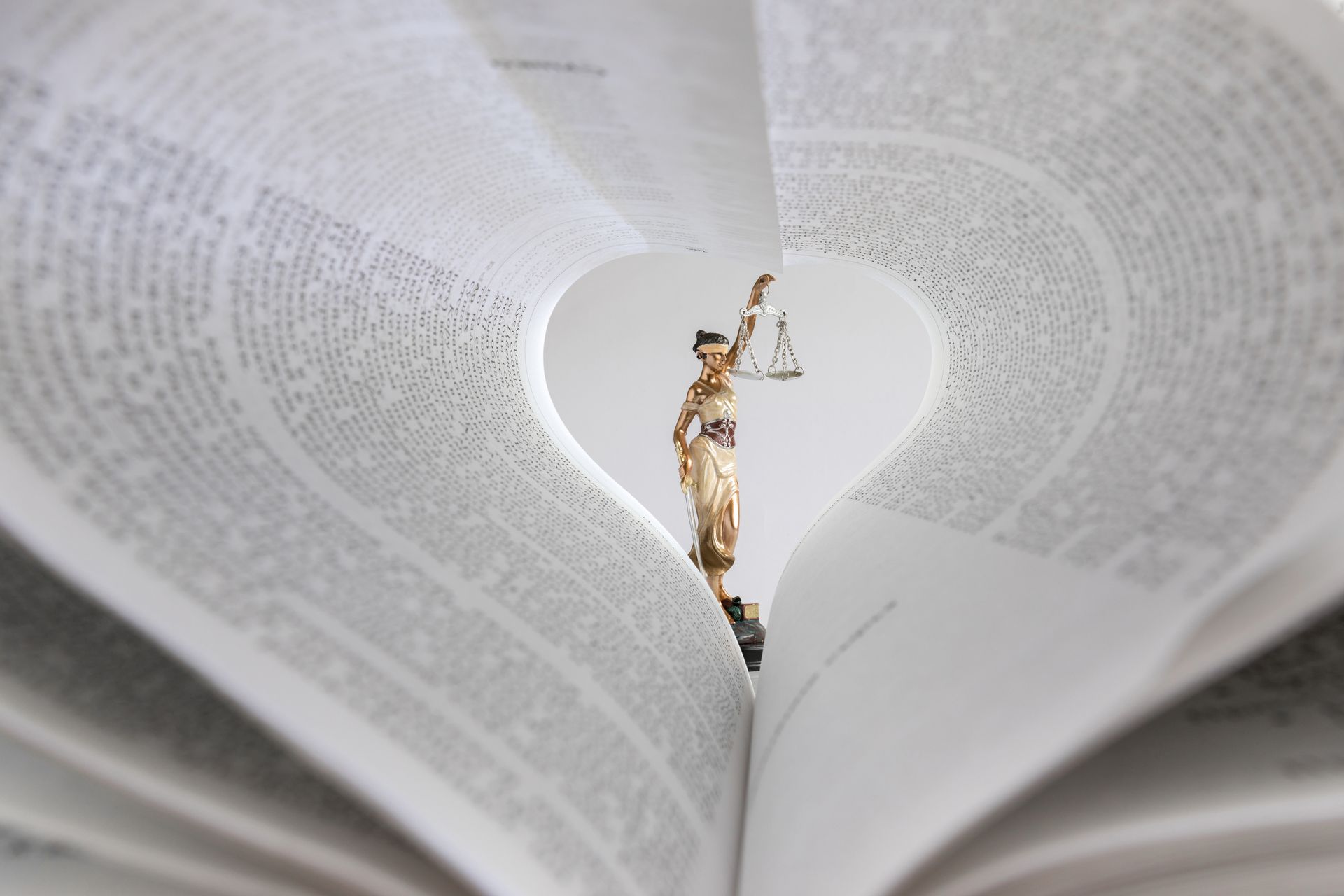 Une petite statue de la Justice tenant une balance, visible à travers une ouverture dans les pages d'un livre en forme de cœur.