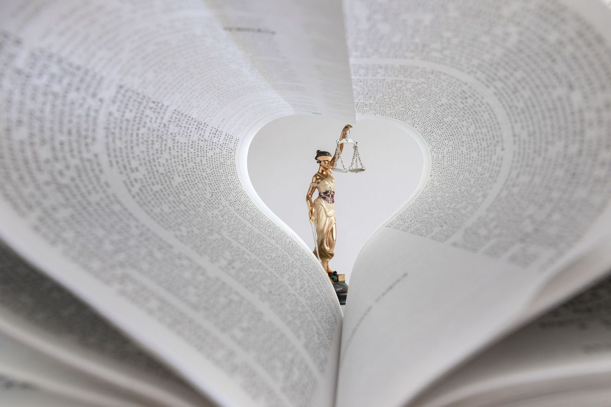 Une petite statue de la Justice tenant une balance, visible à travers une ouverture dans les pages d'un livre en forme de cœur.