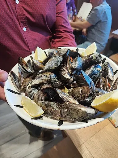Una persona sostiene un plato de mejillones con rodajas de limón.