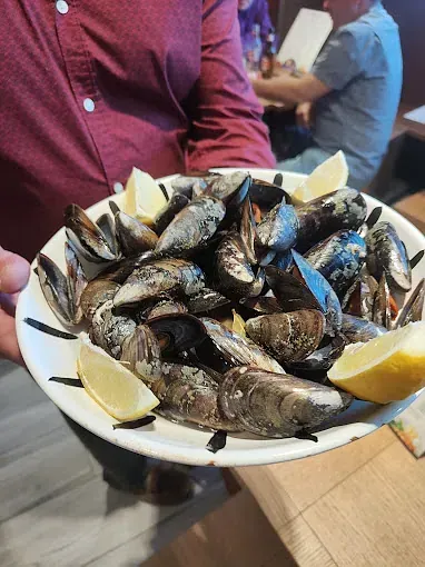 Una persona sostiene un plato de mejillones con rodajas de limón.