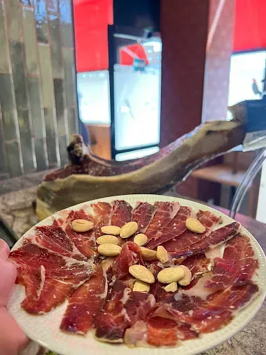 Una persona sostiene un plato de carne y nueces sobre una mesa.