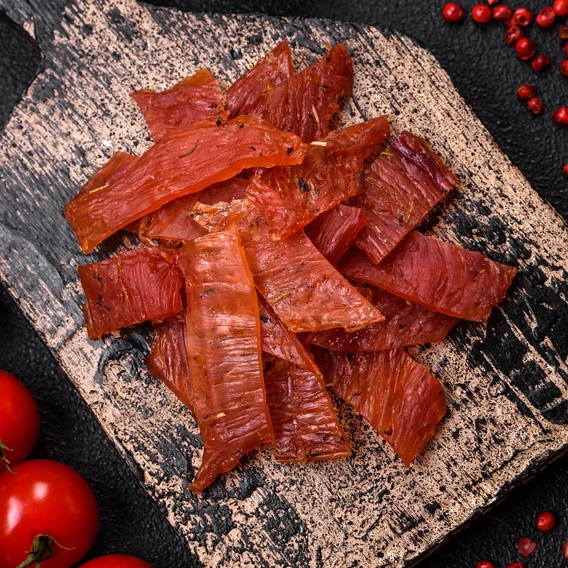 Una pila de cecina reposa sobre una tabla de cortar de madera.