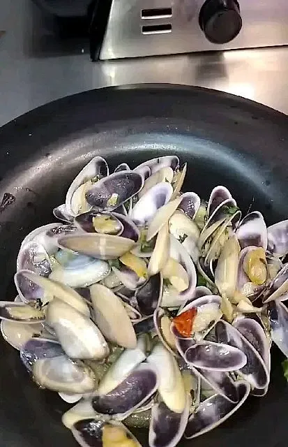 En una estufa se cocina una sartén llena de almejas y ajo.