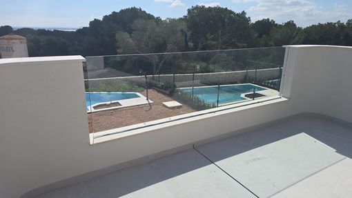 Patio con paredes blancas con vistas a una piscina y una cancha de tenis bajo un cielo despejado.