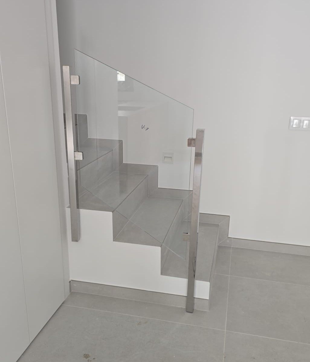 Barandilla de cristal en una escalera de un luminoso pasillo interior con escalones y suelo de baldosas grises.