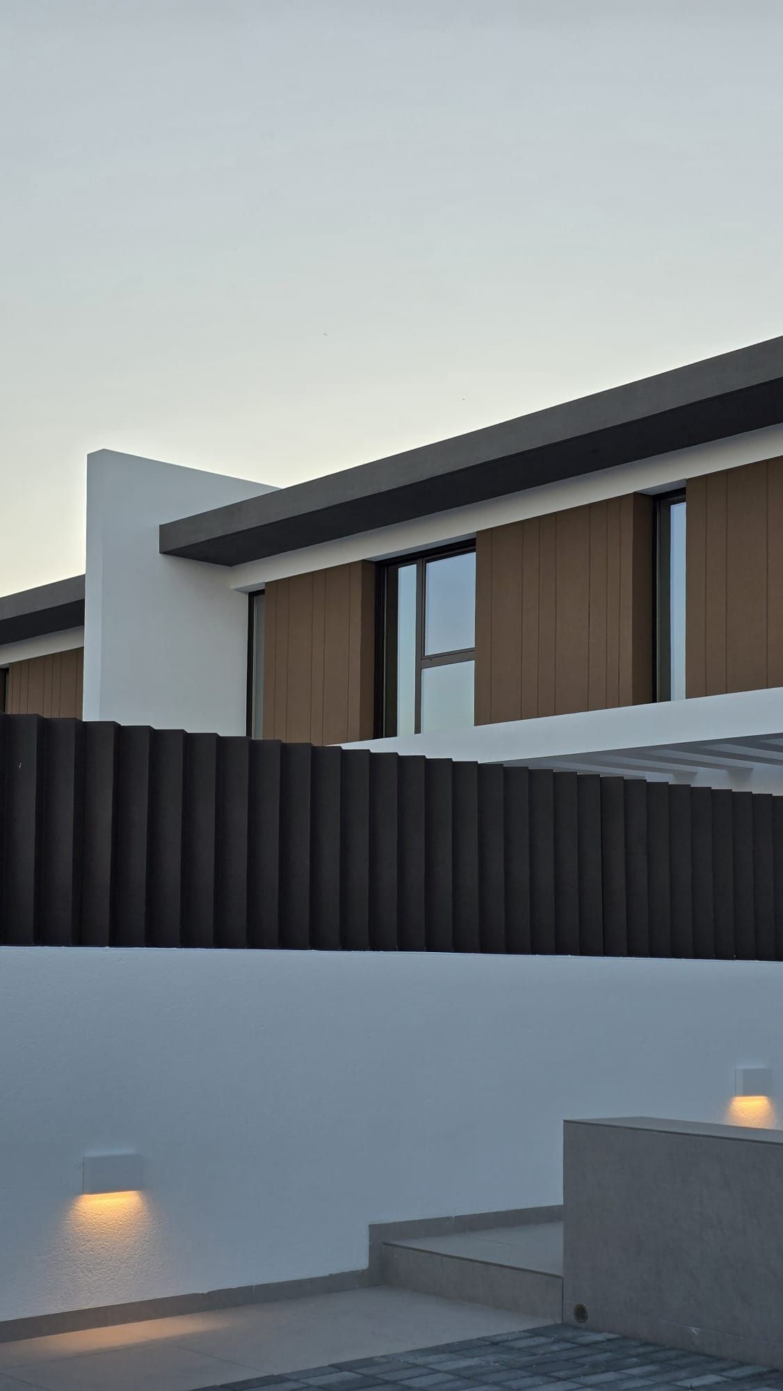 Exterior de una casa moderna con valla oscura, paredes blancas, contraventanas de madera.