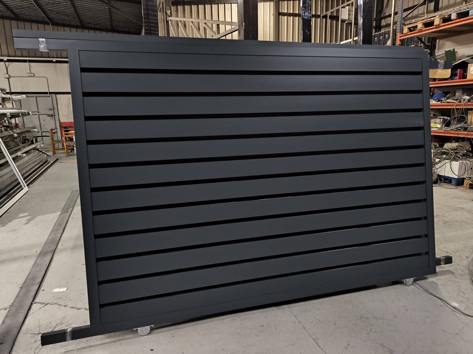 Panel metálico negro con lamas situado en un taller o almacén.
