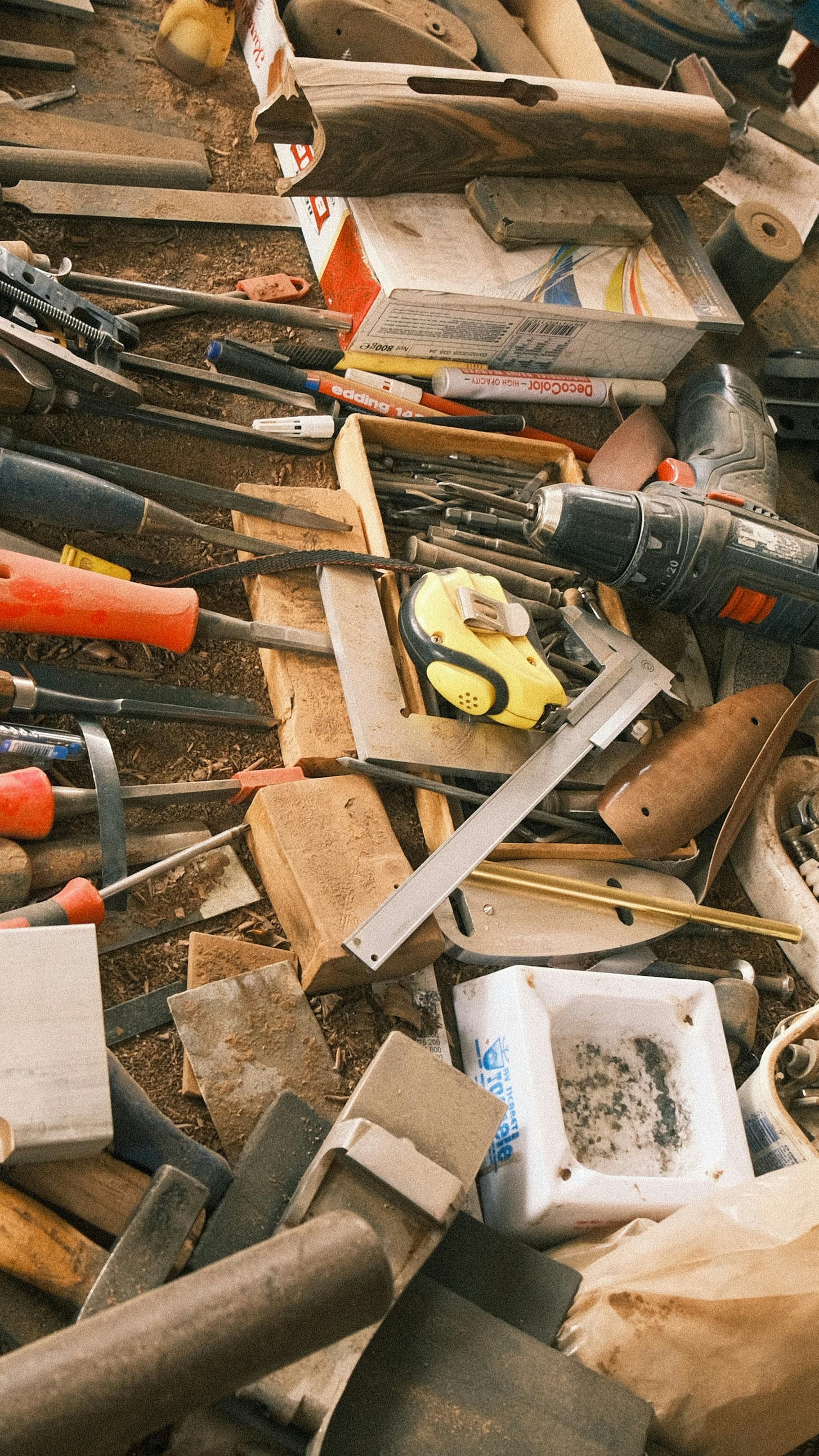 Montón de herramientas variadas y restos de madera esparcidos sobre una superficie de trabajo tosca.