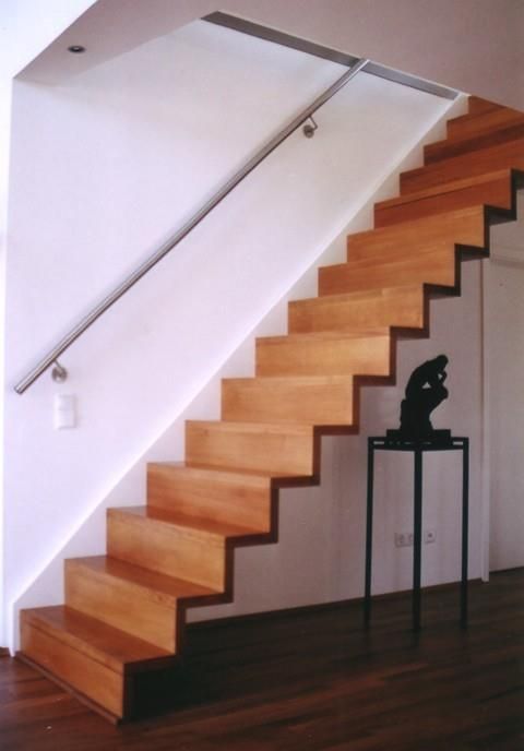Eine Holztreppe mit einem Metallgeländer und einer Statue auf einem Ständer darunter