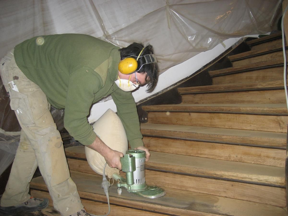 Ein Mann mit Kopfhörern und Maske, der eine Holztreppe schleift