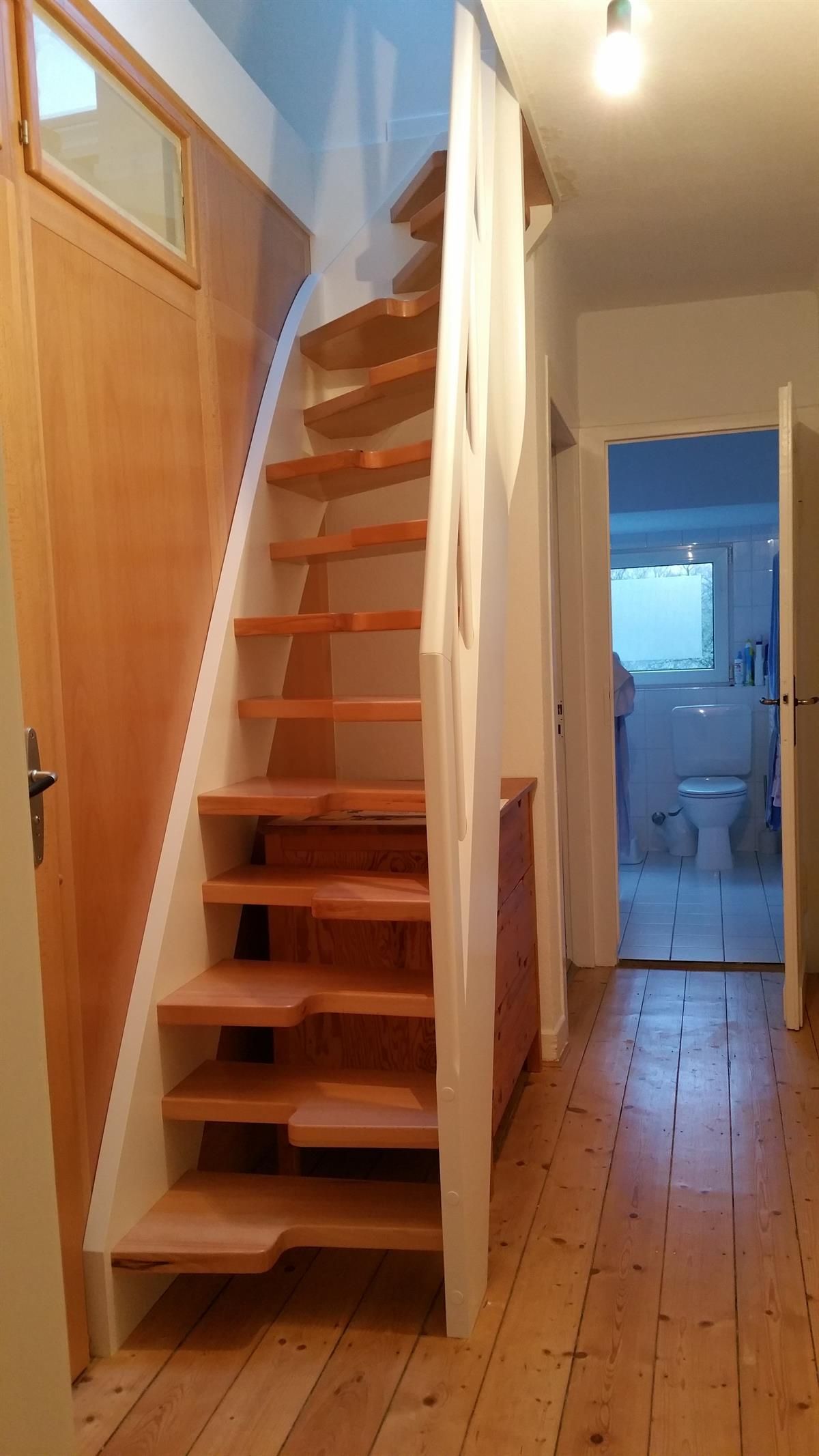 Eine Holztreppe in einem Flur, die zu einem Badezimmer führt