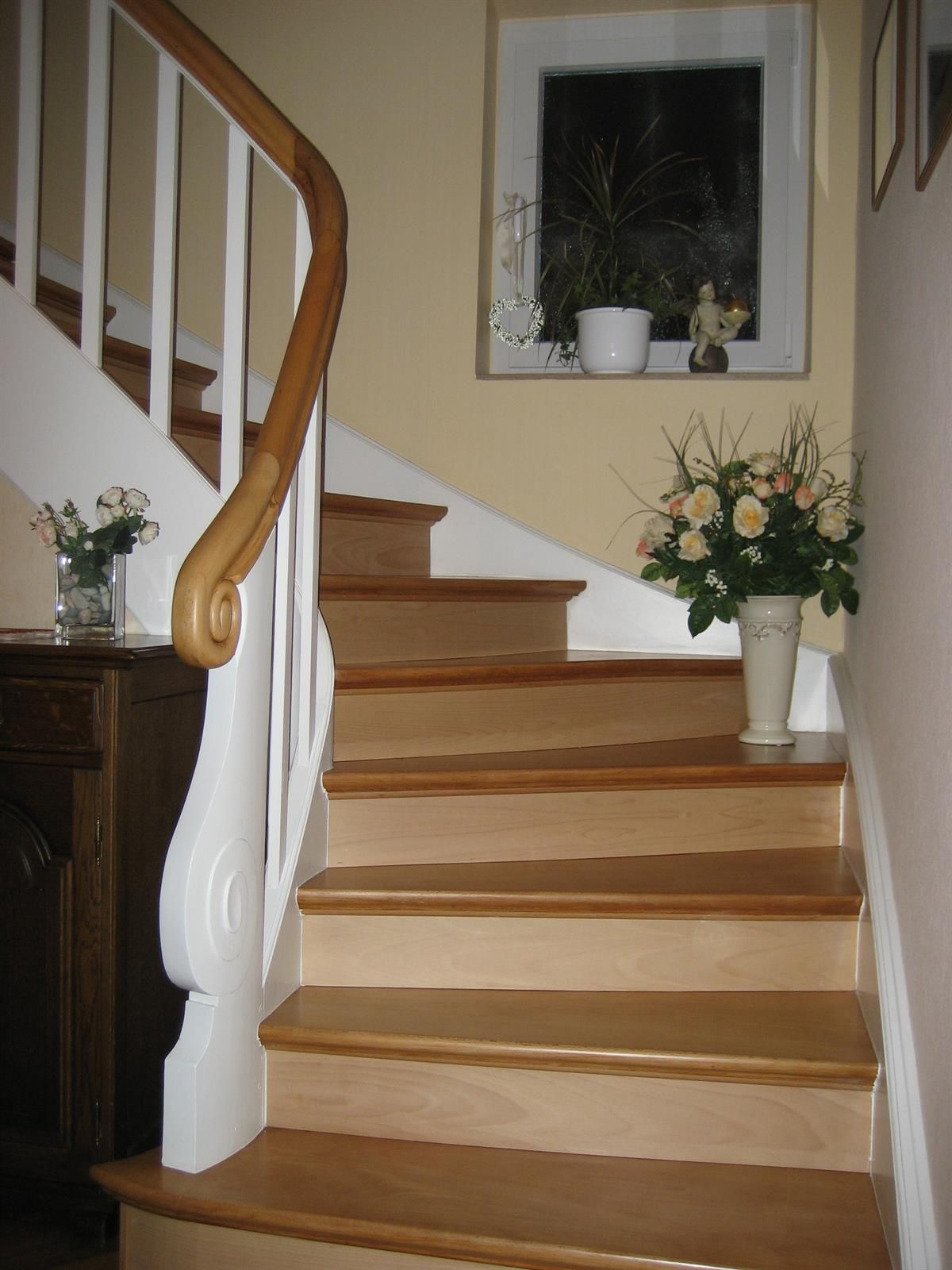 Eine Holztreppe mit weißem Geländer und einer Vase mit Blumen auf den Stufen