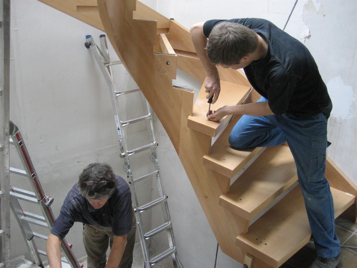 Zwei Männer arbeiten auf einer Holztreppe mit einer Leiter im Hintergrund.