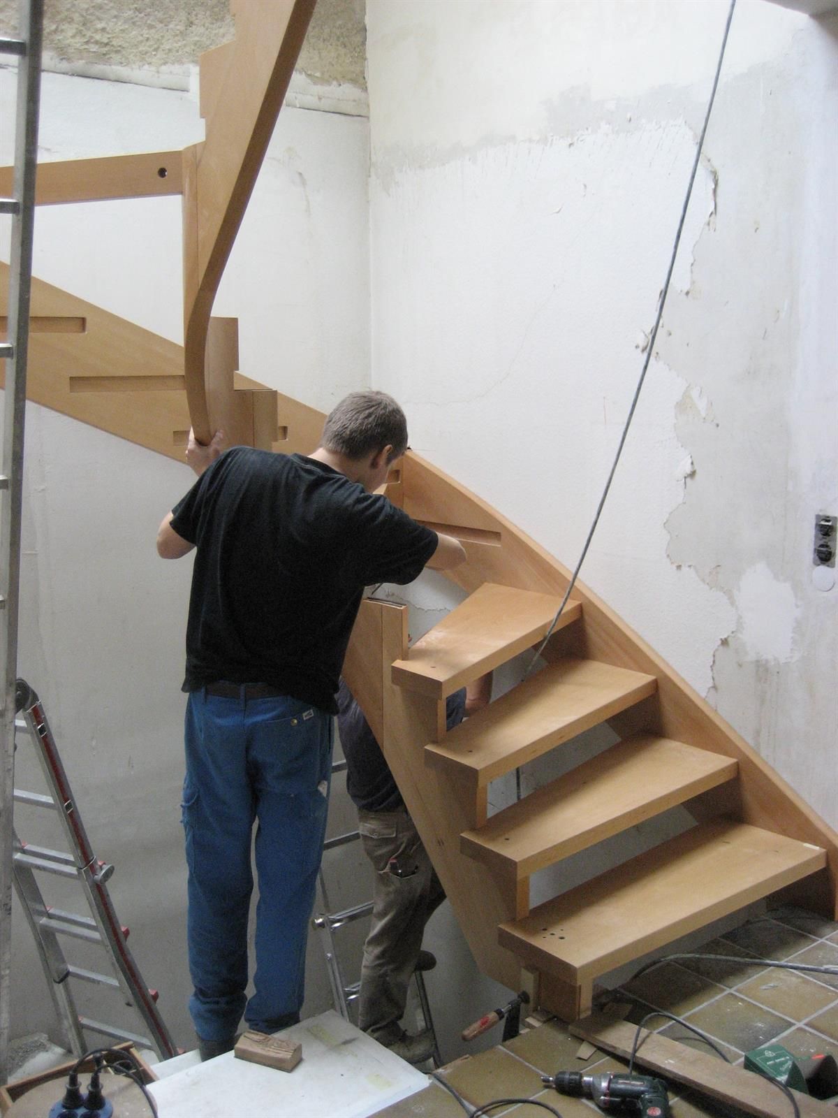 Ein Mann im schwarzen Hemd arbeitet an einer Holztreppe