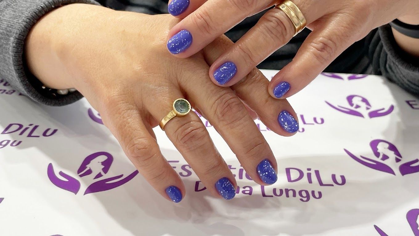 Una mano de mujer con uñas moradas y un anillo de oro.