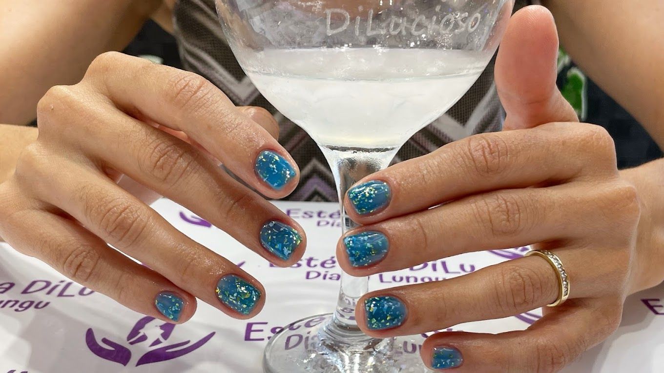 Una mujer con uñas azules sostiene una copa de vino.