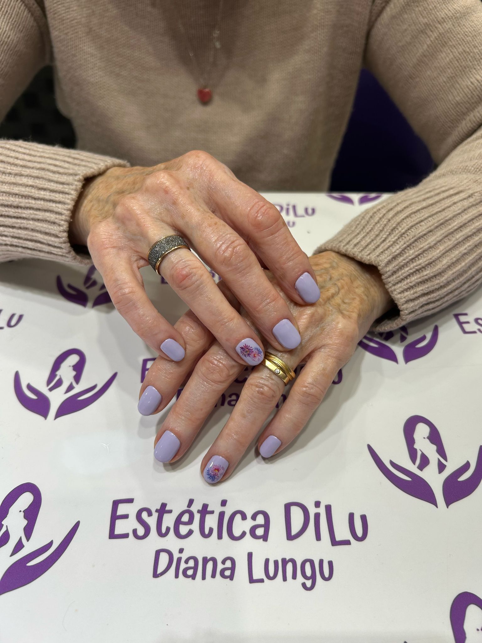 Una mujer con uñas moradas está sentada en una mesa con las manos juntas.