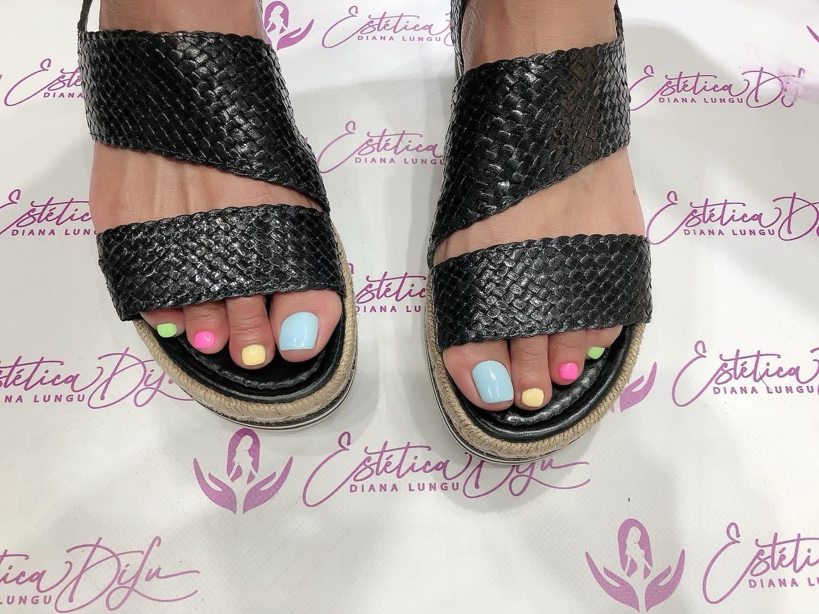Pies de mujer con esmalte de uñas de colores y sandalias negras.