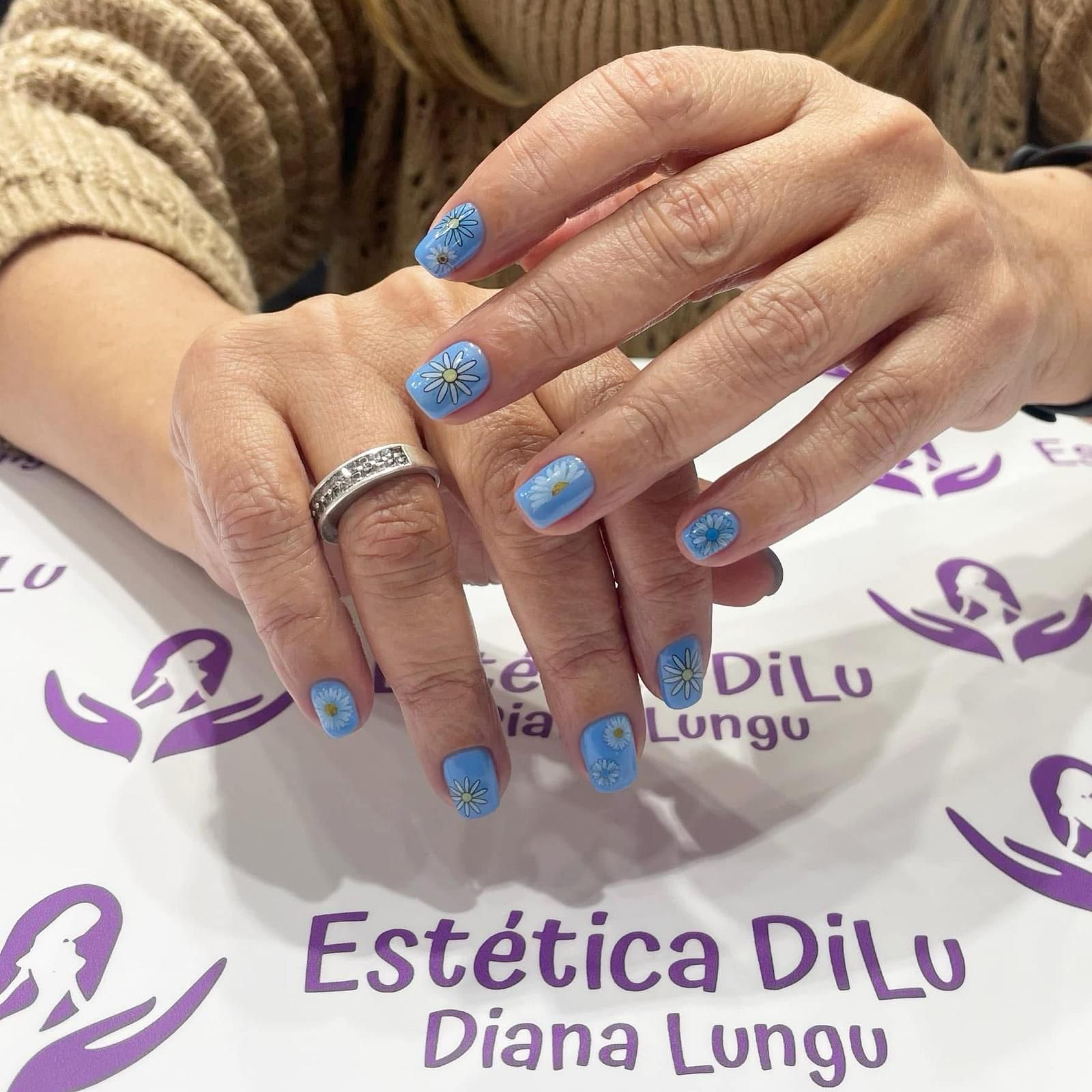 Las manos de una mujer con uñas azules y un anillo en el dedo.