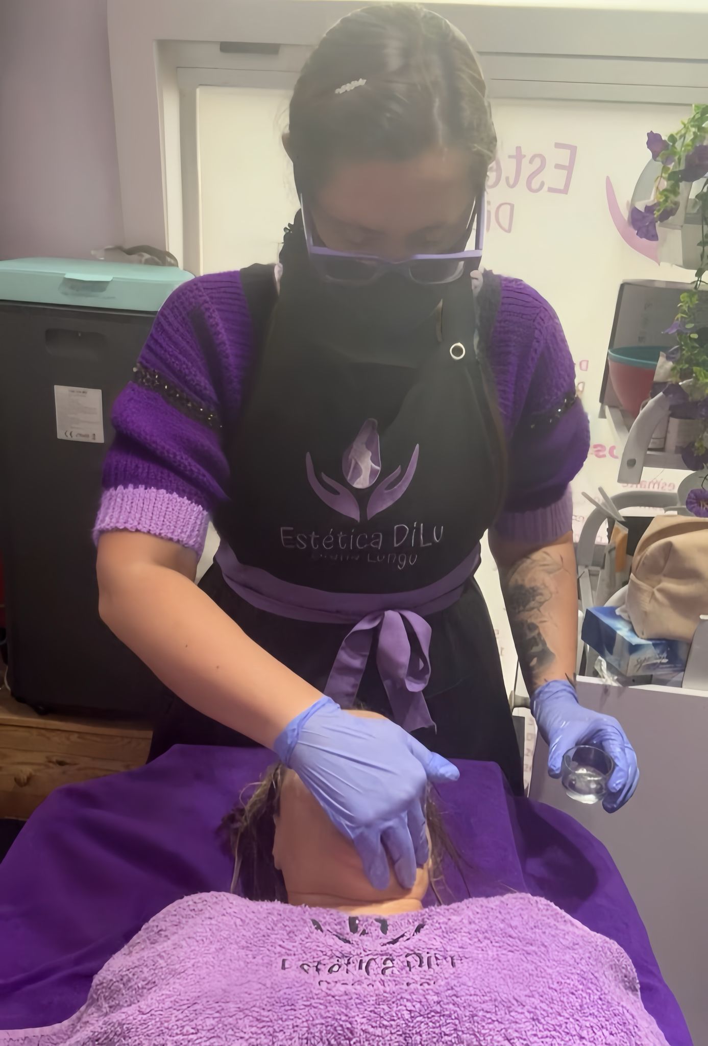 Una mujer que lleva una máscara y guantes le está dando a una mujer un tratamiento facial.