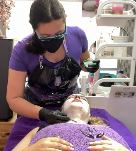 Una mujer que lleva una máscara le está haciendo un tratamiento facial a otra mujer.