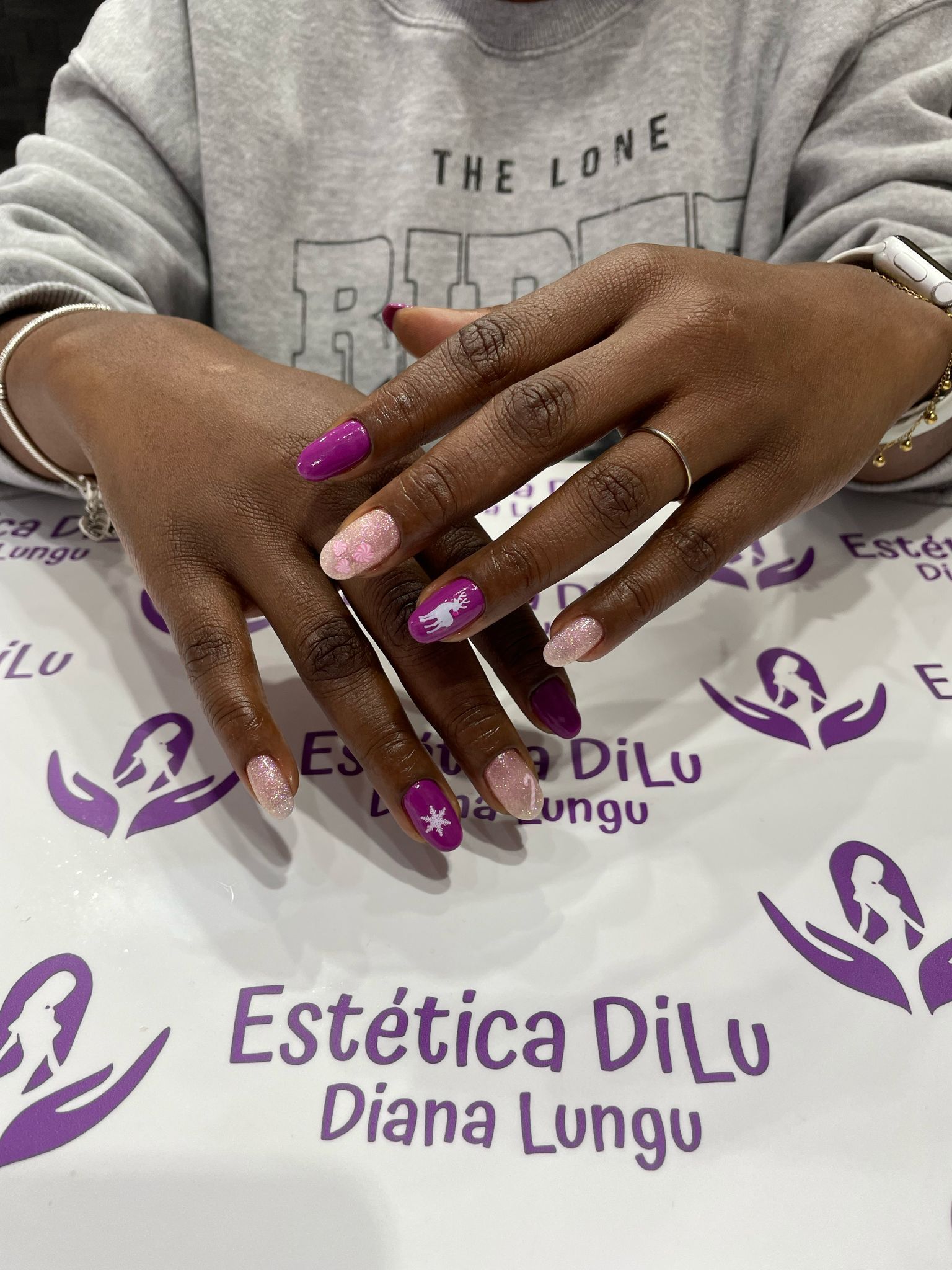 Una mujer está sentada en una mesa con las manos juntas y las uñas pintadas de morado y rosa.