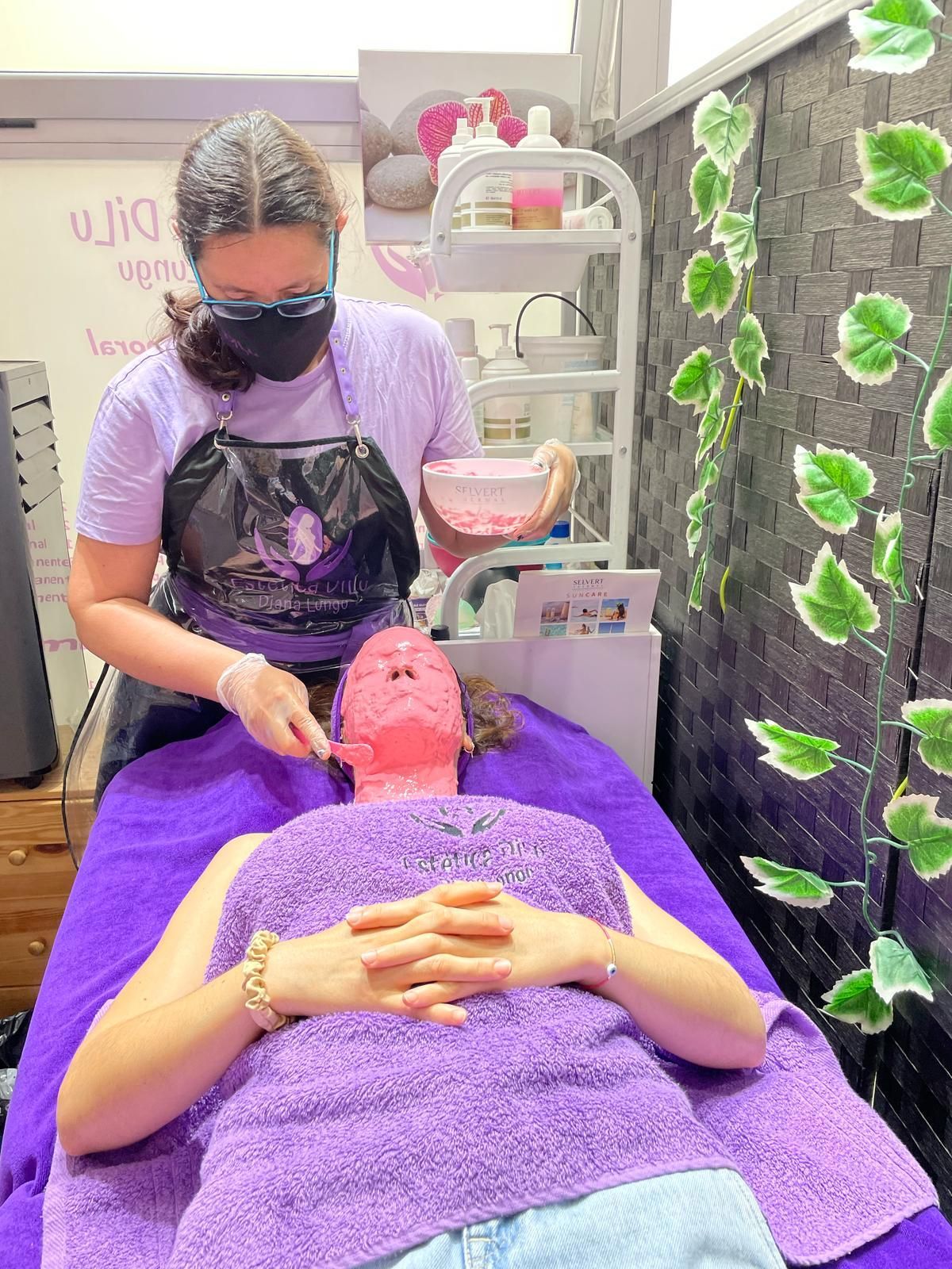 Una mujer está acostada en una cama morada recibiendo un tratamiento facial.