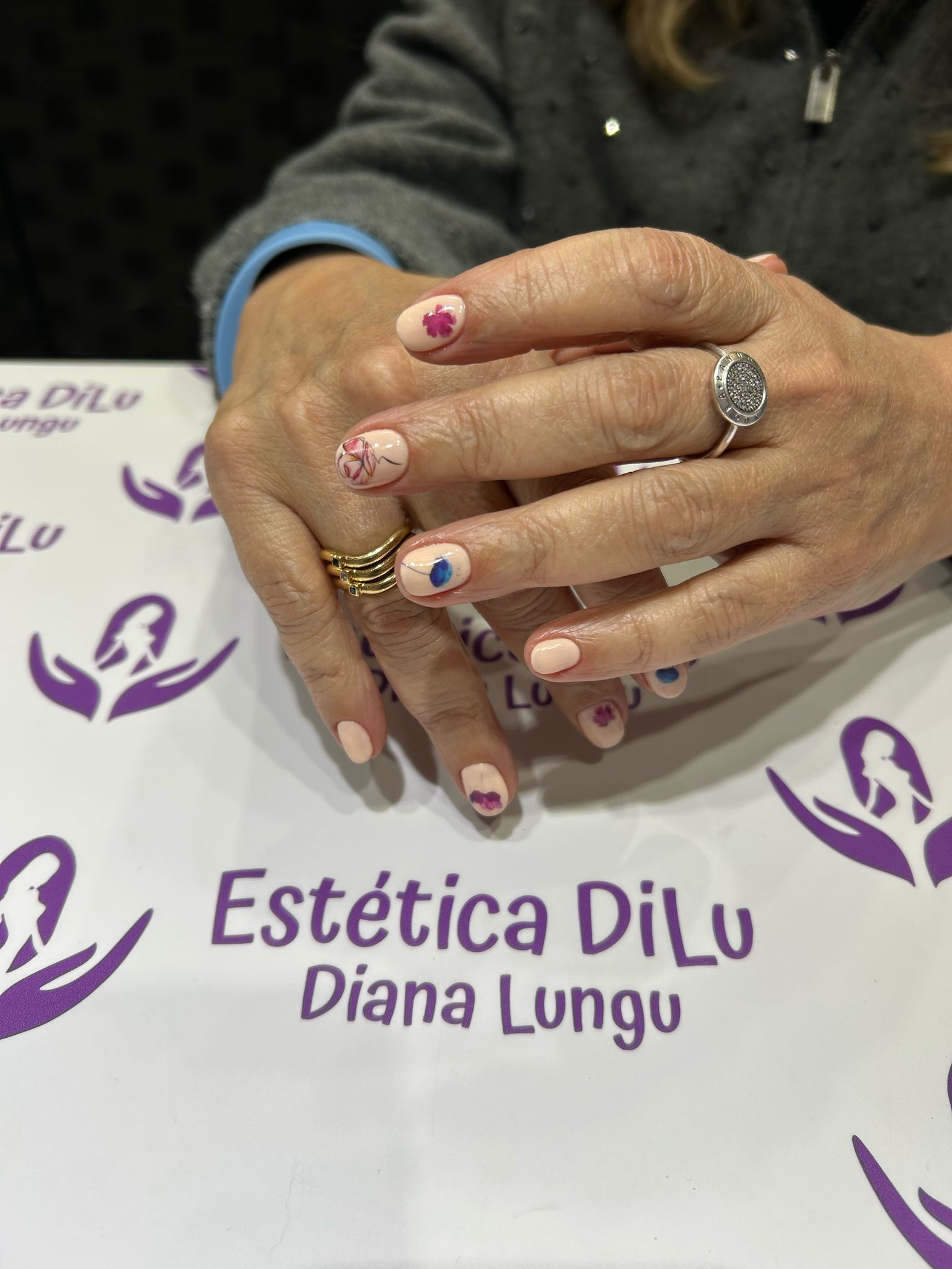 Una mujer está sentada en una mesa con las manos juntas frente a un cartel que dice estetica dilu diana lungu