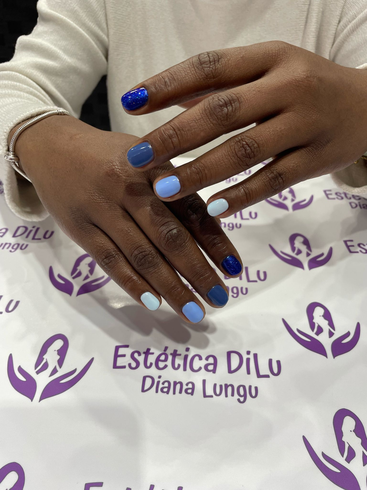 Las uñas de una mujer están pintadas de azul y blanco en un salón llamado estética dilu