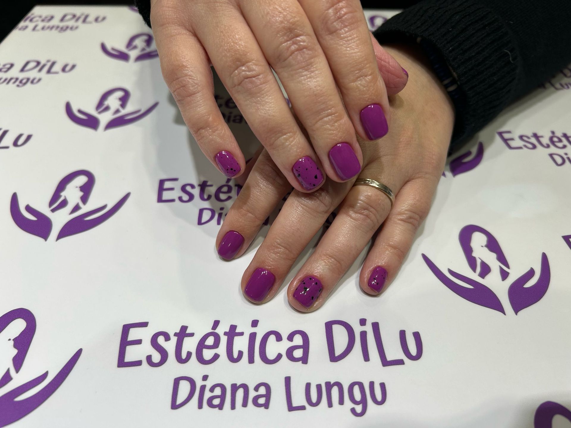 Las uñas de una mujer están pintadas de morado en un salón llamado Estetica Dilu Diana Lungu