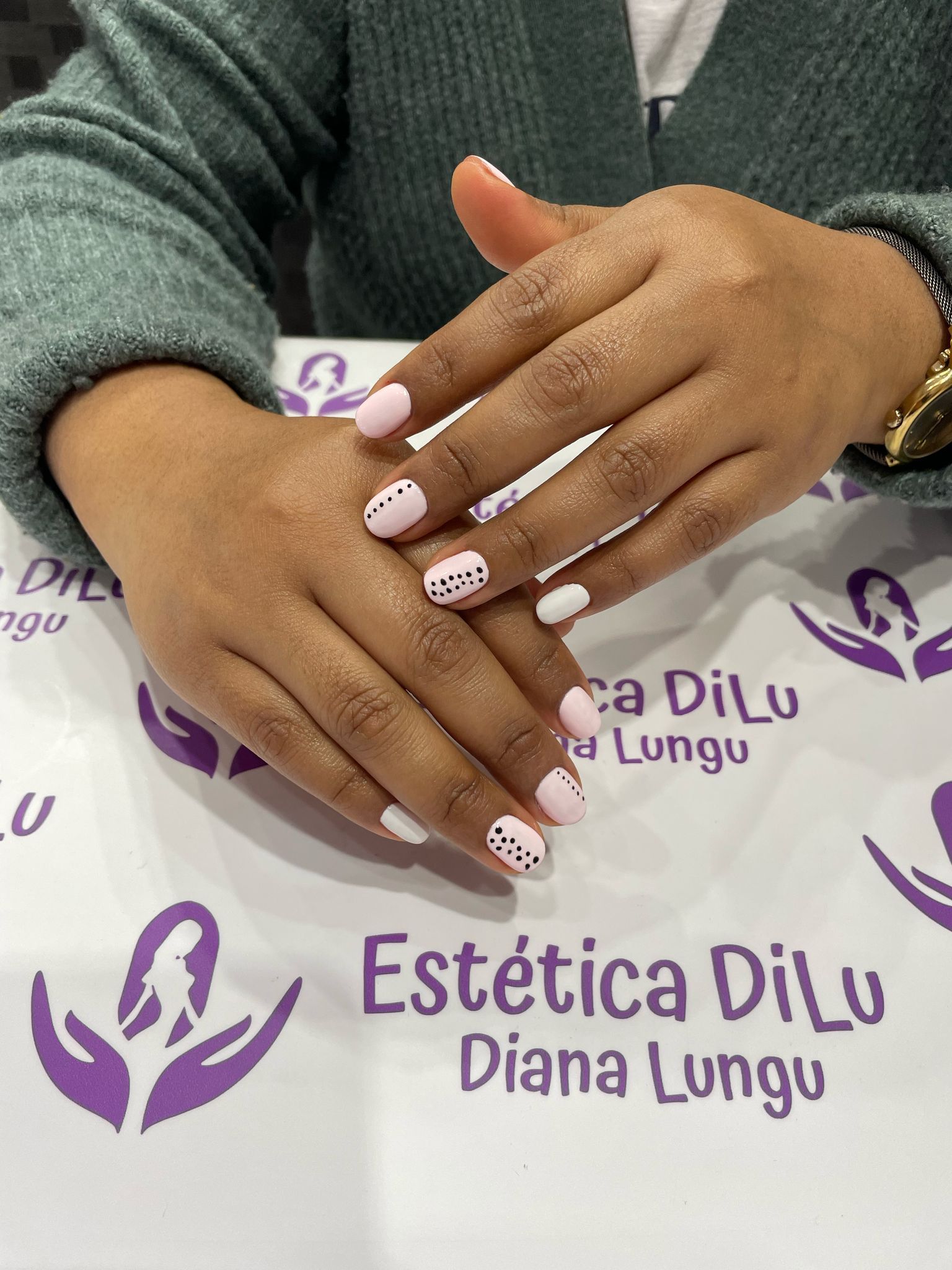 Una mujer está sentada en una mesa con las manos juntas frente a un cartel que dice estetica dilu diana lungu