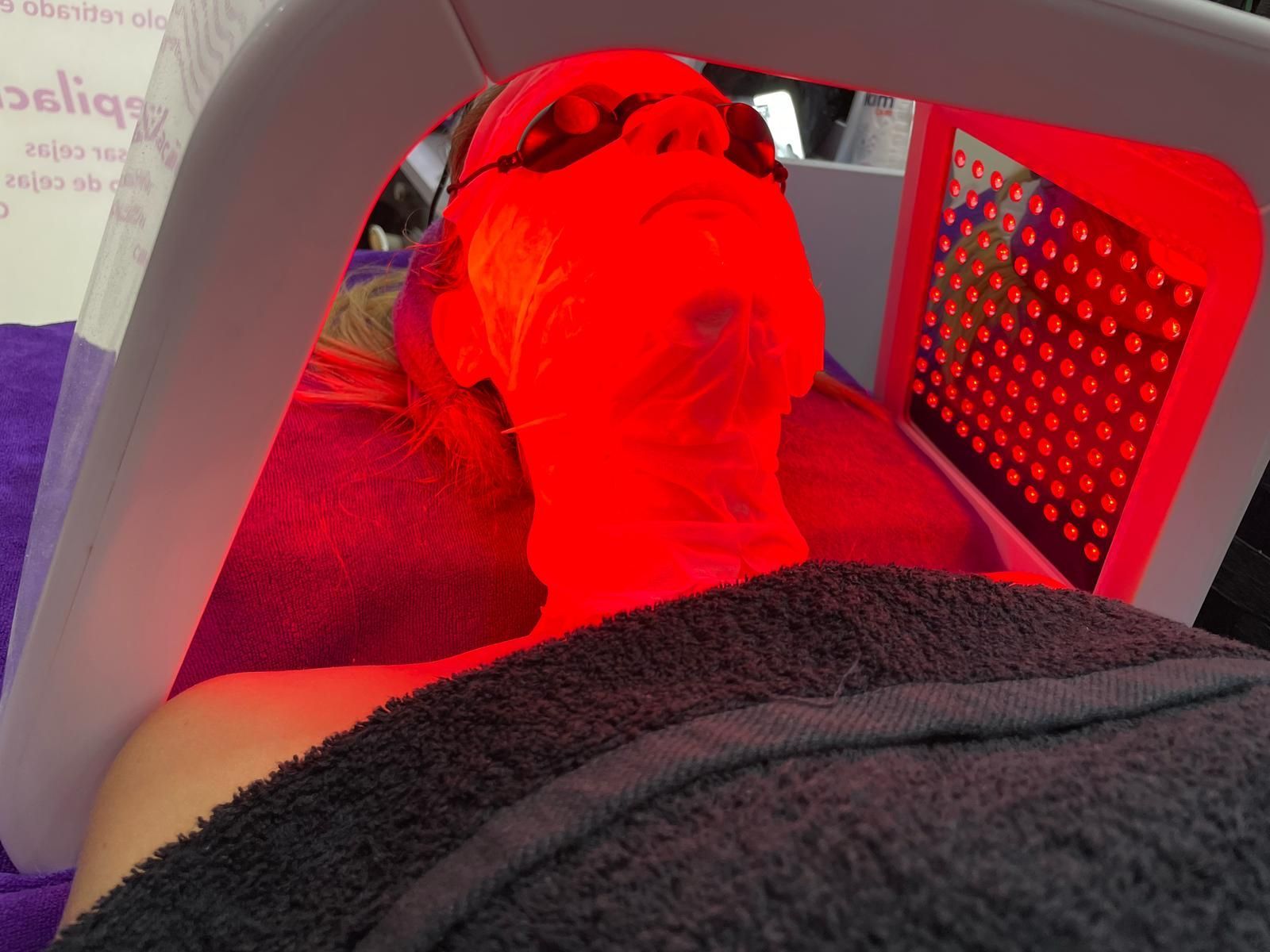 Una mujer recibe un tratamiento de luz roja en su cara.