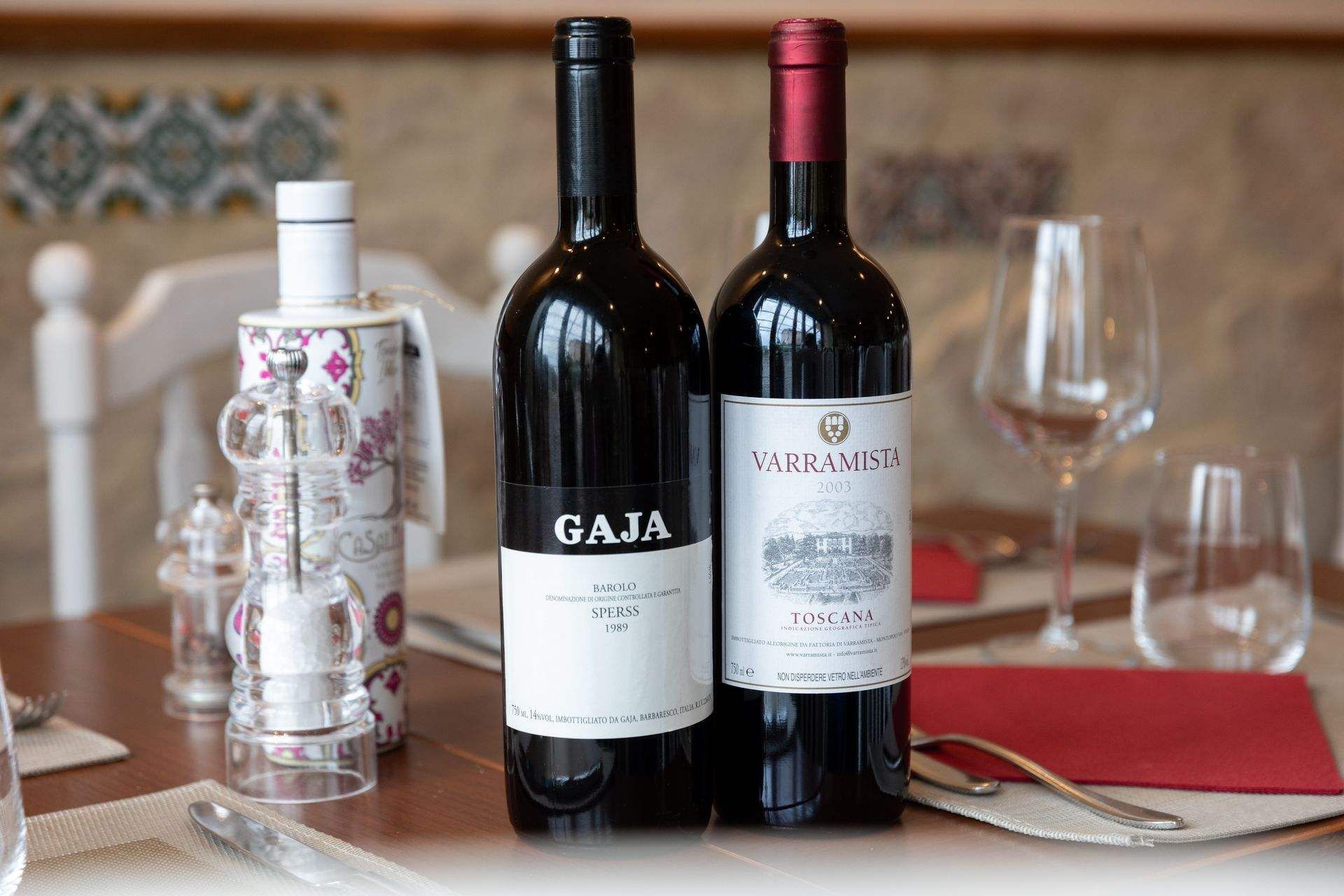 Deux bouteilles de vin rouge sur une table avec des verres et des condiments, ambiance restaurant.